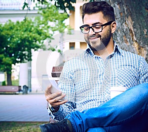 Businessman sitting on park bench with coffee using mobile phone.