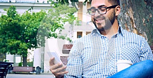 Businessman sitting on park bench with coffee using mobile phone.