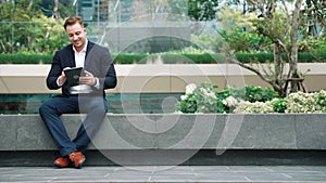 Businessman sitting at park while working on tablet by reading report. Urbane