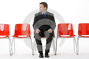 Businessman Sitting In Row Of Empty Chairs