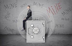 Businessman sitting on safe and background of wall with inscription `Mine`.