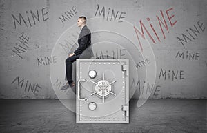 Businessman sitting on safe and background of wall with inscription `Mine`. photo