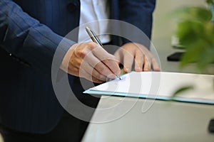 Businessman sitting at shiny office desk signing a contract with noble pen