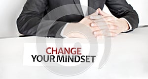 Businessman sitting at the table and signboard with text Change Your Mindset