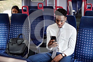 Businessman Sitting In Train Commuting To Work Checking Messages On Mobile Phone