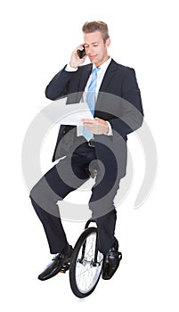Businessman Sitting On Unicycle Talking On Cellphone