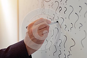 Businessman sketching many question marks on office whiteboard