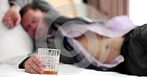 Businessman sleeping on bed holding glass of whiskey