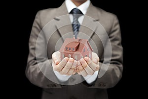 Businessman with small brown house over black background