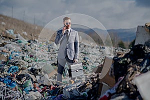 Businessman with smartphone on landfill, consumerism versus pollution concept.