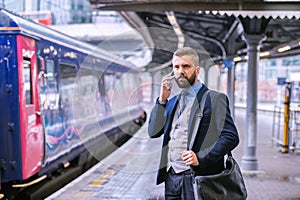 Businessman with smartphone, making a phone call, train platform