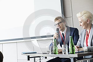 Businessman speaking through microphone while sitting at desk in convention center