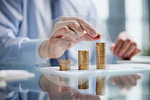 Businessman stacking coins on table, business growth concept. Hand puts coin to stack.