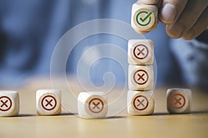 Businessman stacking green correct sign mark on top of Red Cross mark which print screen on wooden cube block for approve and