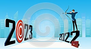 Businessman stand on 2022 lettering and shooting arrow bow to arrow target in 2023 year