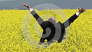 Businessman stand with back in blossom field and lift hands up, successful