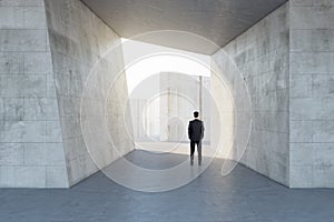 Businessman standing in abstract concrete tile space interior background with sunlght. Design concept