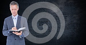 Businessman standing against black wall and writing on diary