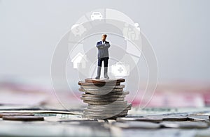 Businessman standing on coins stacking with donut chart and insurance icons include family healthcare house piggy saving and car