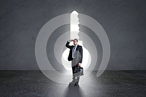 Businessman standing in concrete interior with abstract bright keyhole opening. Success and leadership concept