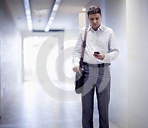 Businessman standing in the corridor and looking down at his phone