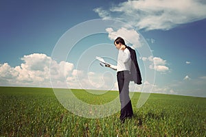 Businessman standing on a field with a blue sky and reads the ne