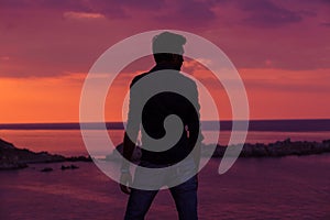 Businessman standing in front of the sea at sunset