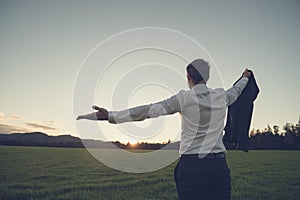 Businessman standing in green meadow looking towards the sunset