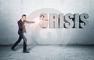 Businessman standing on ground hitting word 'CRISIS' with fist