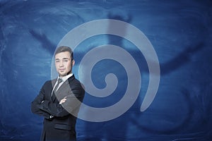 Businessman standing with hands across and his shadow on blue blackboard behind him tail like devil