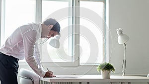 Businessman standing at his office desk leaning in to sign a contract