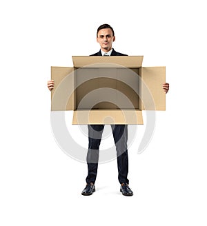 Businessman standing and holding big open empty light beige cardboard mail box in his hands, isolated on the white