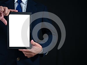 Businessman standing holding white screen tablet on dark background. Advertising concept. Banner sign