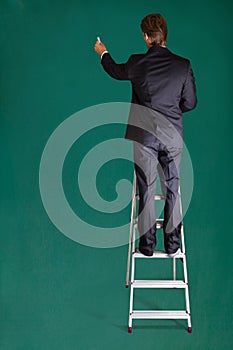 Businessman Standing On Ladder Writing On Chalkboard