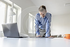 Businessman standing leaning on his desk reading a tablet compu