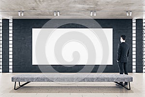 Businessman standing in modern gallery interior and looking on empty billboard