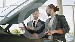 Businessman standing near open front trunk thinking about buying car. Salesperson with client in the car showroom near