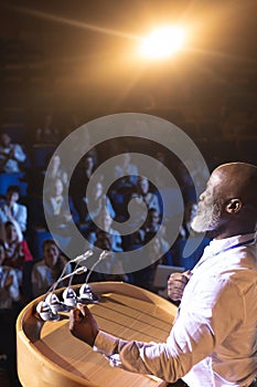Businessman standing near podium and giving speech to the audience in the auditorium