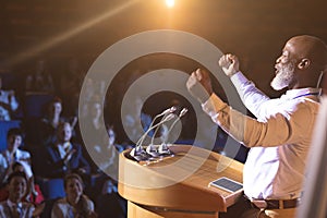 Businessman standing near podium and giving speech to the audience in the auditorium