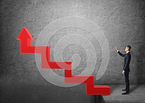 Businessman standing near stairs in the form of red arrow pointing upwards.