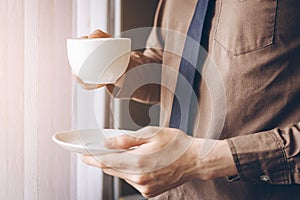 Businessman standing near window and holding coffee cup relax while working