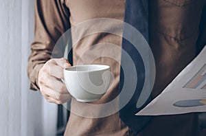 Businessman standing near window holding coffee and paper sheet vintage tone