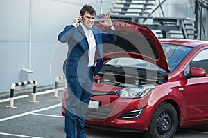 Businessman standing next to broken car and calling in service