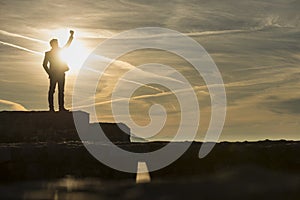 Businessman standing outdoors on a wall with his fist raised against a sun