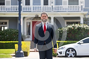 Businessman standing outside a modern house. Real estate concept. Agent ready to sell home.