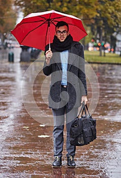 Businessman standing in the rain outdoors with umbrella