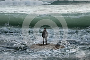Businessman standing on rock in the ocean facing oncoming waves