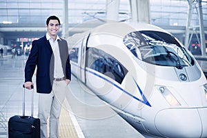 Businessman standing with a suitcase on the railroad platform by a high speed train in Beijing