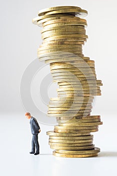 Businessman standing under risky coin stack.