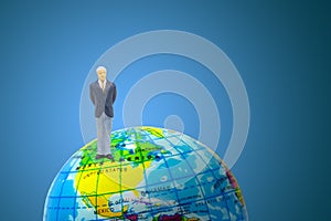 Businessman standing on world globe toy in blue background.